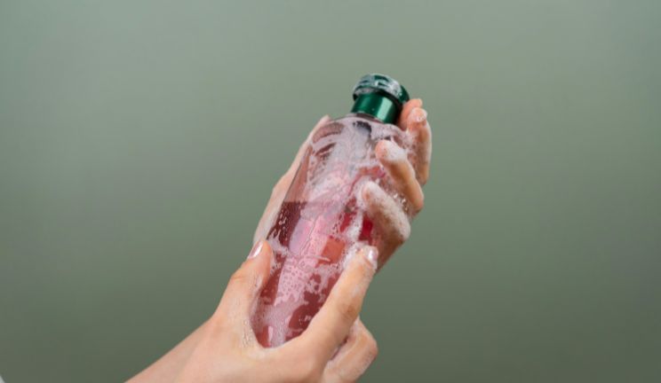 A pair of hands. They have foam. They are holding a shampoo bottle